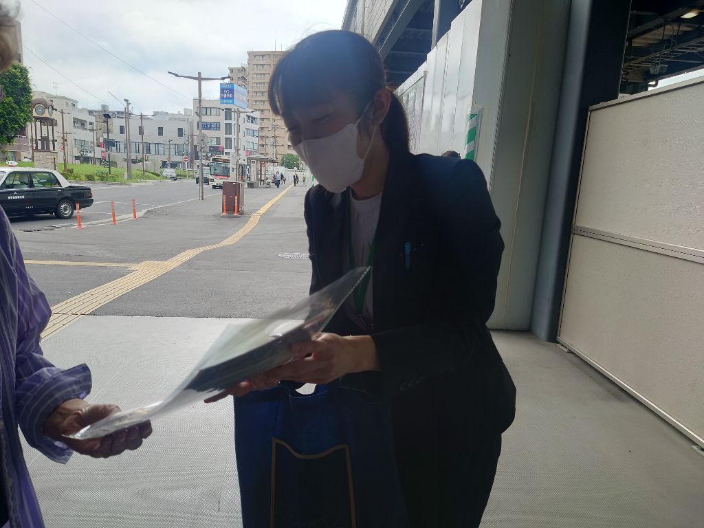 銀行職員が駅利用者に啓発品を渡す様子