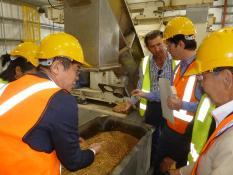 アルタス再生可能エネルギー事業所内を視察する訪問団の写真。出来上がった燃料用ペレットを実際に手に取りながら説明を受けている。