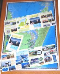 フレーザーコースト市に関するパンフレットの写真。フレーザーコースト市の地図の上に、表紙が見えるように畳まれているパンフレット1枚と、表と裏のそれぞれの全ページが見えるように広げられたパンフレット2枚が乗っている。