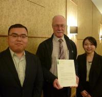 共栄大学から贈られた親書を持つ男性と二人の学生の写真