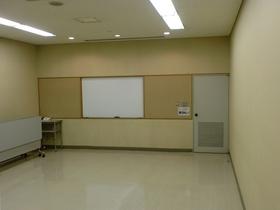 ホワイトボードが真ん中にあり右奥に灰色のドアがある会議室102内を撮影した写真