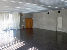 大きな窓にかけられた白色のカーテンから光が差し込むコンクリート壁の市民ホール内を撮影した写真