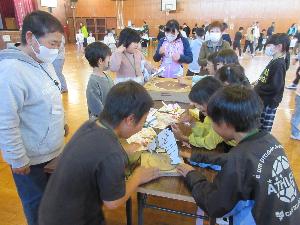 昔遊びで地域の方と児童が紙相撲をしている写真