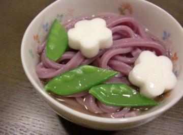 どんぶり鉢に入った紫色のうどんの上に絹さやえんどう豆などの具がのっているふじうどんの写真