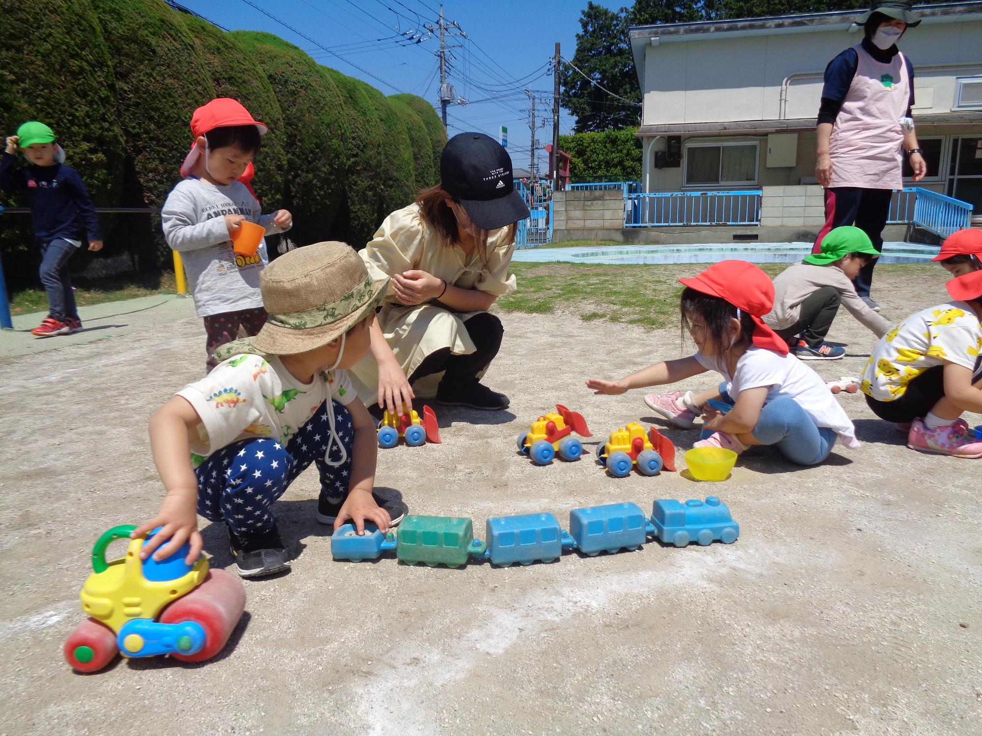 所庭で汽車の玩具をつなげて遊ぶ親子