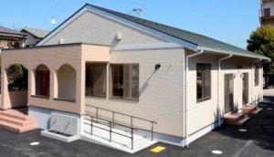 三角屋根で外壁が肌色の建物の、備後放課後児童クラブの外観の写真