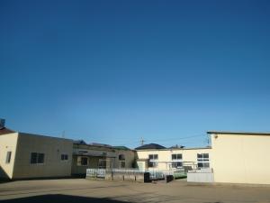 雲一つない晴天の下建つ白色の外壁の春日部市立第3保育所外観を遠目のアングルから撮影した写真