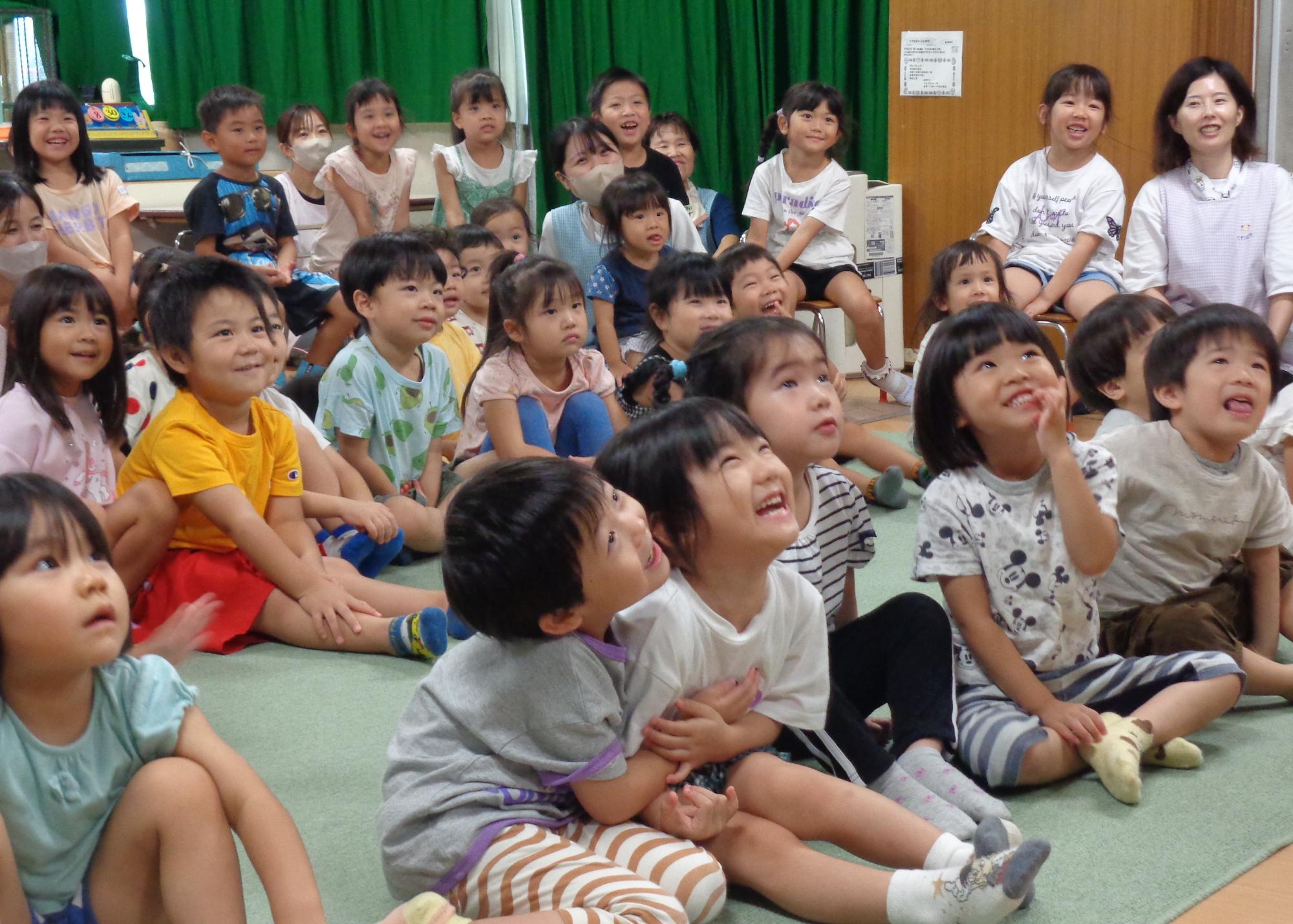 かみをつかったたのしいおはなしをみて笑いあうこども達