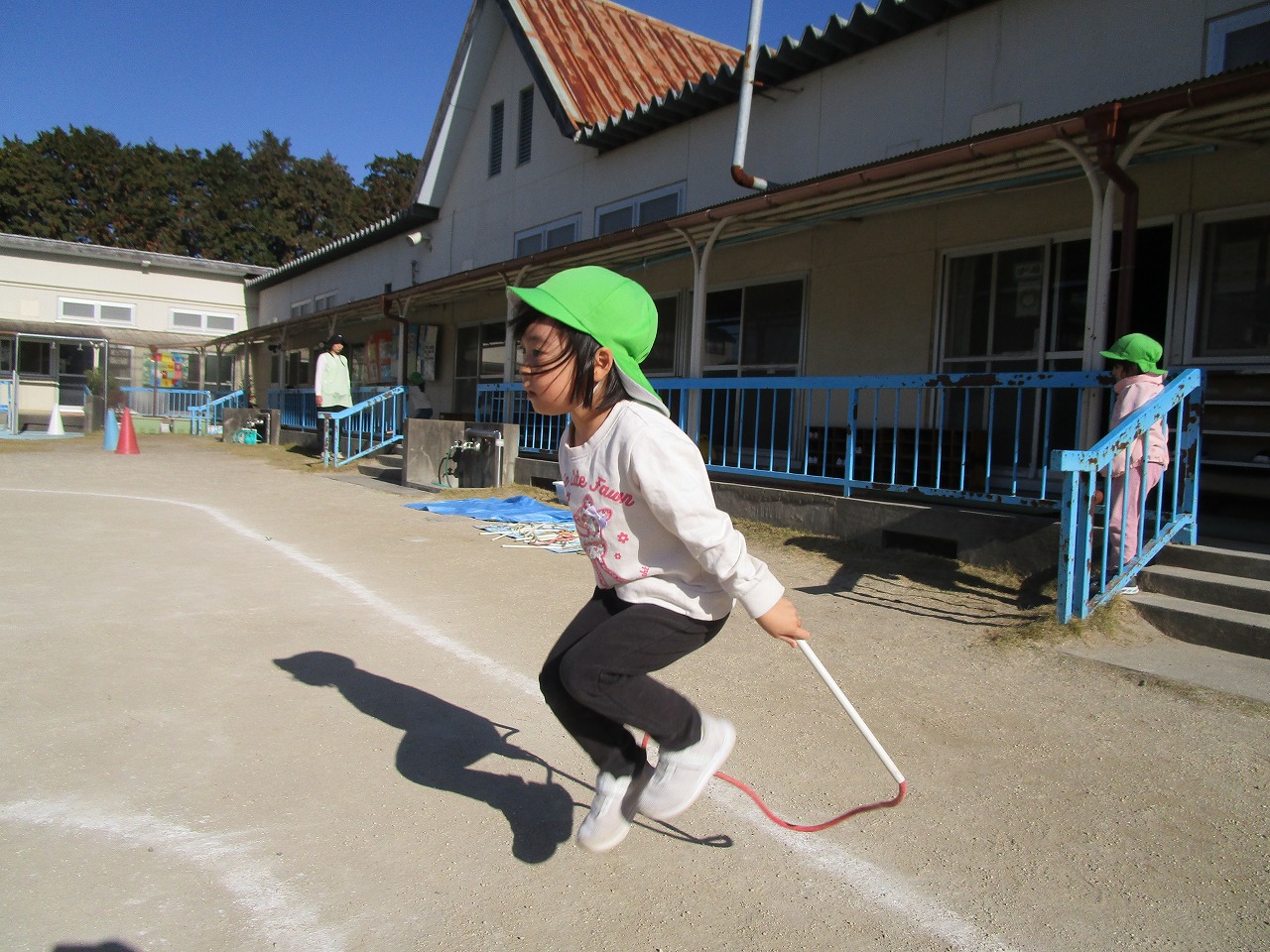 黄緑色の帽子をかぶり、ひとり一生懸命縄跳びをしようとしている園児の写真