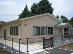 ワイヤーの塀に囲まれた、三角屋根でピンクの外壁の桜川放課後児童クラブの外観の写真