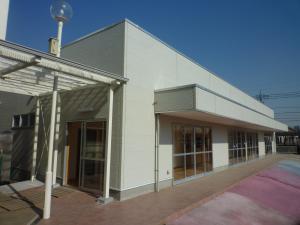 青空の下建つ白壁の春日部市すすむ学園児童クラブの外観を左斜め側から撮影した写真