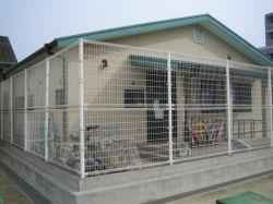 白色のメッシュフェンスに囲まれた緑色の屋根が特徴的な武里西小学校内にある武里西放課後児童クラブの外観を撮影した写真