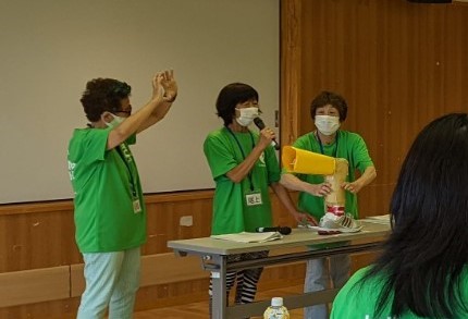 3名のフレイルサポーターがふくらはぎの模型を使って指輪っかテストの説明をする様子