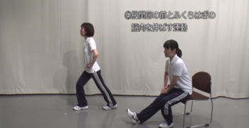 座っている人と立っている人が並んで、足を伸ばす体操をしている写真