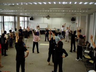 右手を腰に当て、左手を上にあげる体操をしている人たちの写真