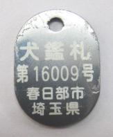 シルバーのプレートに飼い犬として登録されていることを証明するための情報が白の文字で記載されている犬の鑑札の見本写真