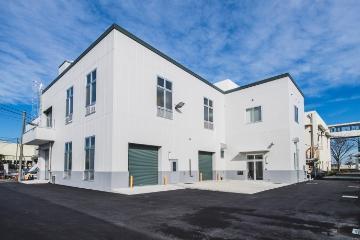 青空の下に白い壁の建物が建っている、施設の東面外観の写真