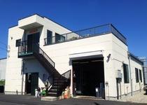 外からも階段で二階にあがれるようになっている株式会社 サンペイントの白い建物の外観写真