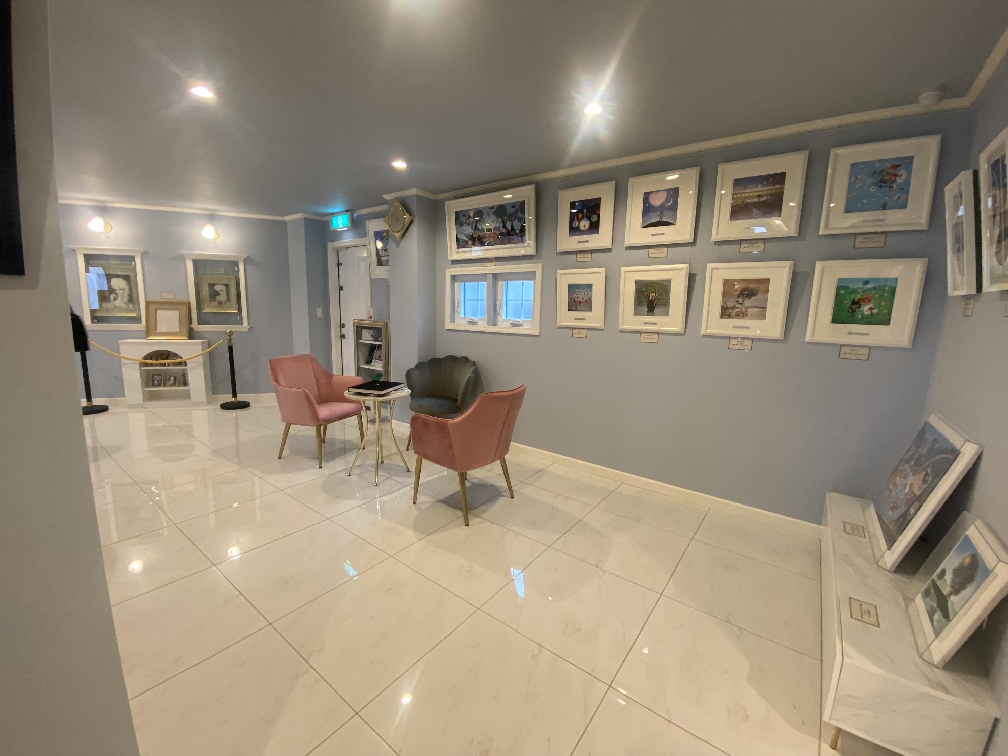 水色の壁に展示された複数の絵とソファとチェアの写真