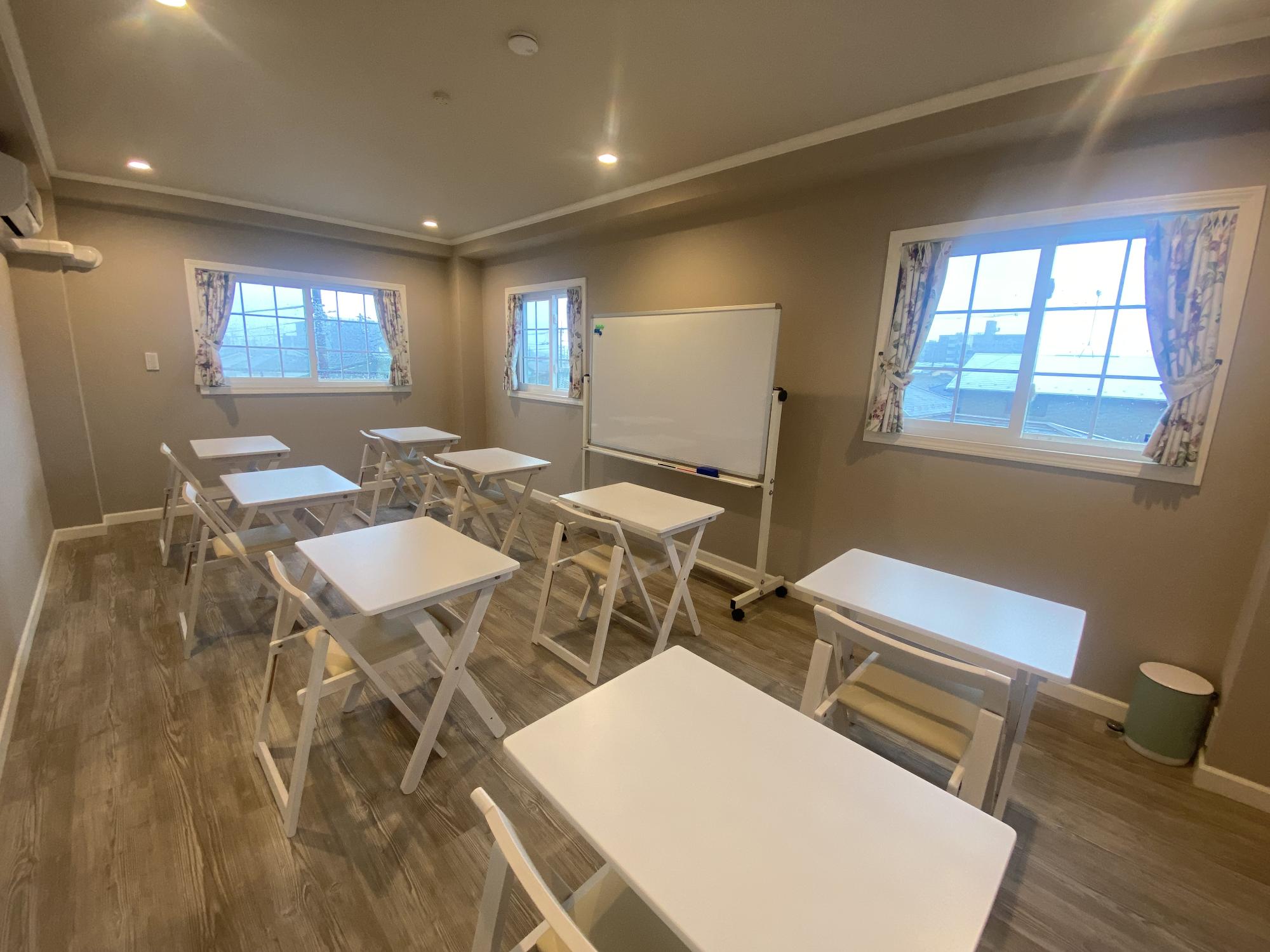 ホワイトボードと洋風なこども向けの机と椅子がある教室のような部屋の写真