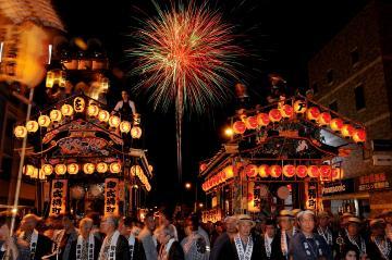 花火の夜空を背景に、神輿の明かりが浮かび上がった鹿沼秋まつりの写真
