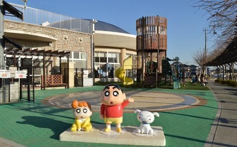 エンゼルドーム外観と、大型遊具を背景にしたクレヨンしんちゃんのモニュメントの写真