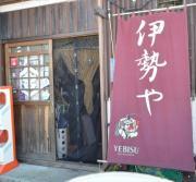 焼き板造りの壁材と赤い暖簾がかかった伊勢や外観の写真