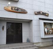 シンプルな白い建物と楕円上の木の看板との組み合わせが特徴的な玩古庵外観の写真