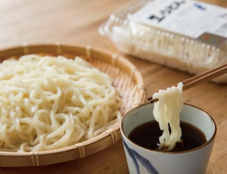 ざるに盛り付けたうどんと手前にはつゆがあり、つゆにうどんをつけている途中の写真