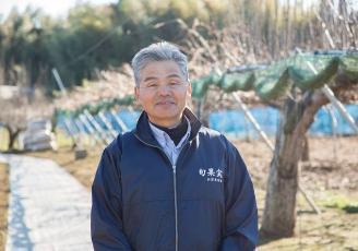 梨園を背景にカメラを見て笑う男性の写真
