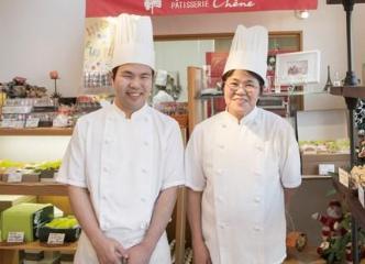 白いエプロン姿でこちらに向かって笑う夫婦の写真