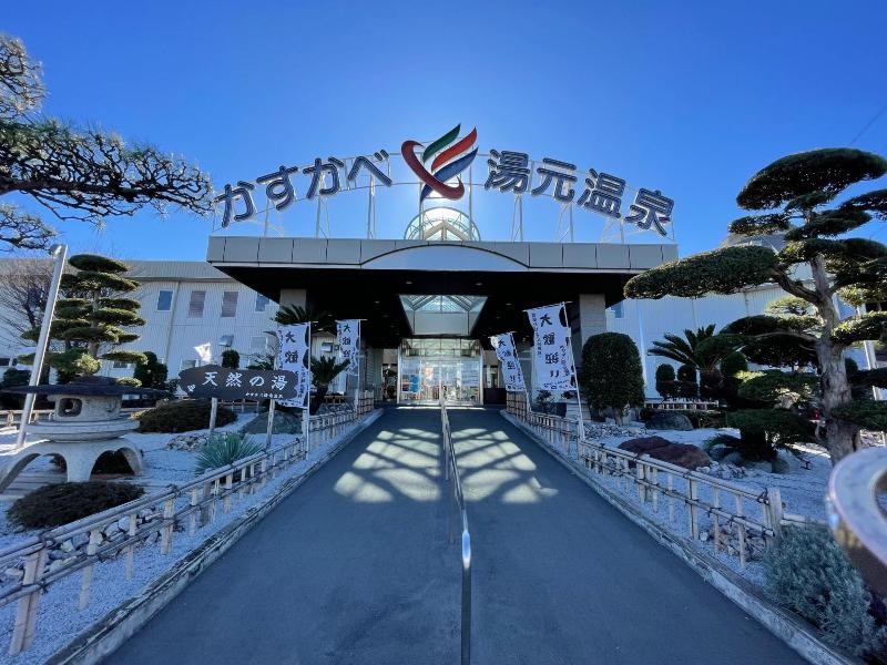 選定された庭木が看板を挟むように生い茂っているかすかべ湯元温泉外観の写真