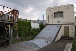 曇り空の下、クリーム色の四角い建物と灰色の半円状の建物が印象的な緑町ポンプ場の外観の写真