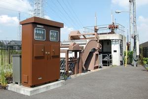 青空の下、メーターが沢山ついた茶色い四角い装置が印象的な三千貝ポンプ場の外観の写真