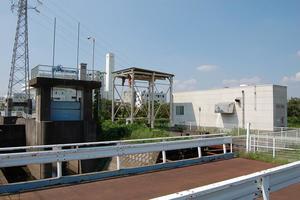 晴れた青空の下、大きな電柱が近くにあり、白い建物とコンクリートでできた施設からなる様子の水角ポンプ場の外観の写真