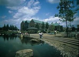 青空の下建つエメラルドグリーン色の屋根が特徴の春日部市役所庄和総合支所を修景池側から撮影した写真