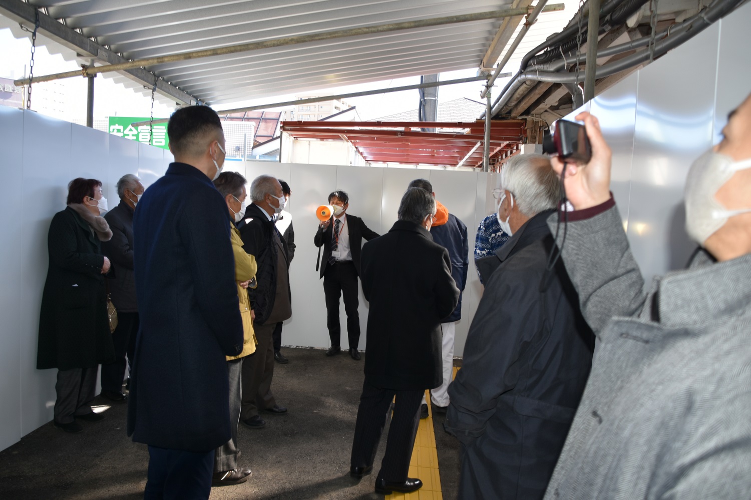 仮駅舎1階からホームへ向かう通路で担当者の説明を受ける同盟会会員一同の写真