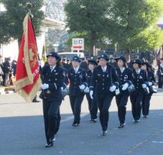 出初式にて先頭に赤い旗を持ち更新する女性消防団員たちの写真