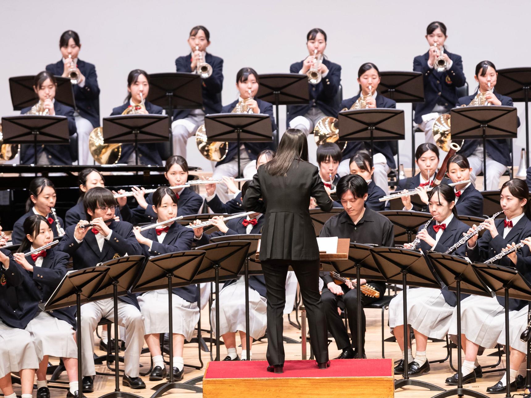 20人ほどの学生が座って吹奏楽を演奏する様子