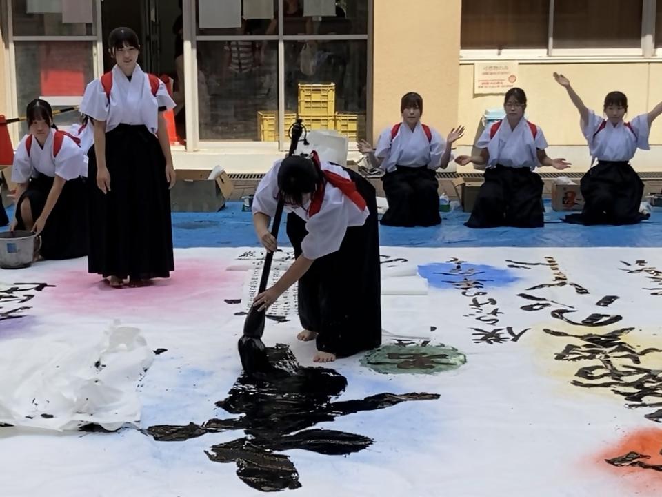 大きな半紙に大きな筆で文字を書く様子