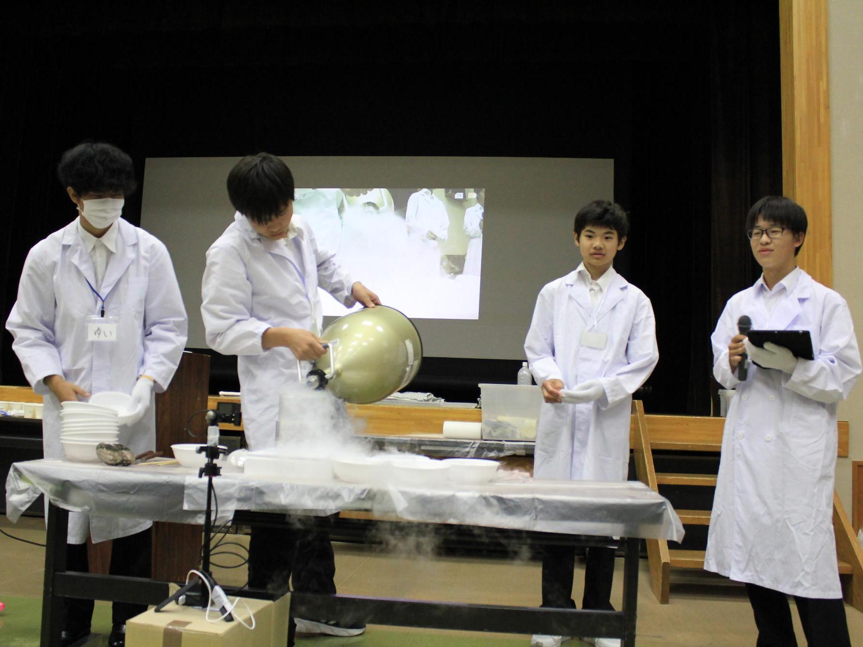 白衣を着た4人の学生が科学実験をする様子