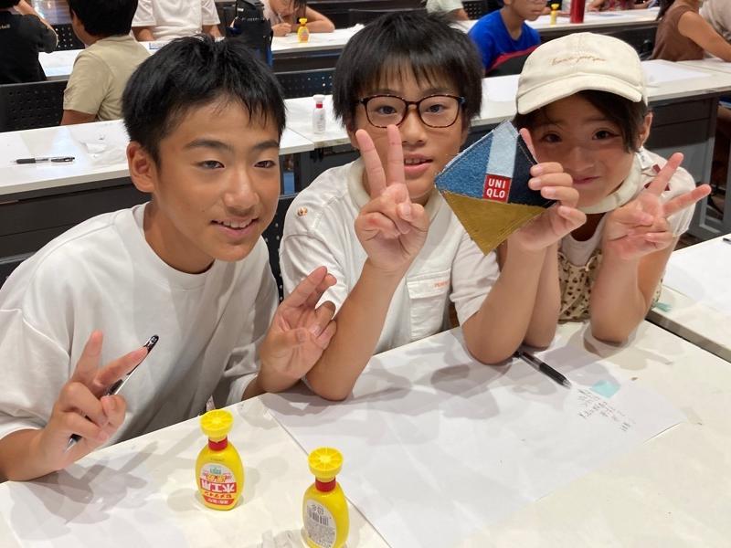 男の子1名が完成したコースターを手に持ち、両脇に別の男の子と女の子がピースして写真撮影する様子