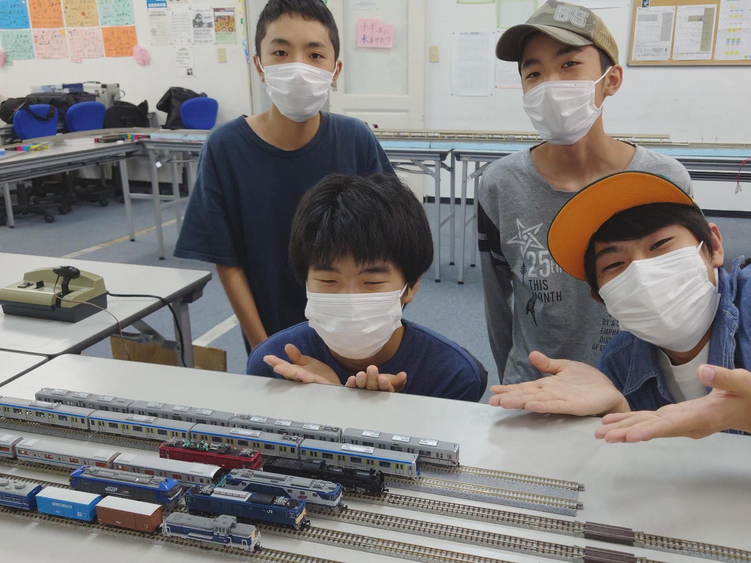 4名の男の子が鉄道模型の前に並ぶ様子