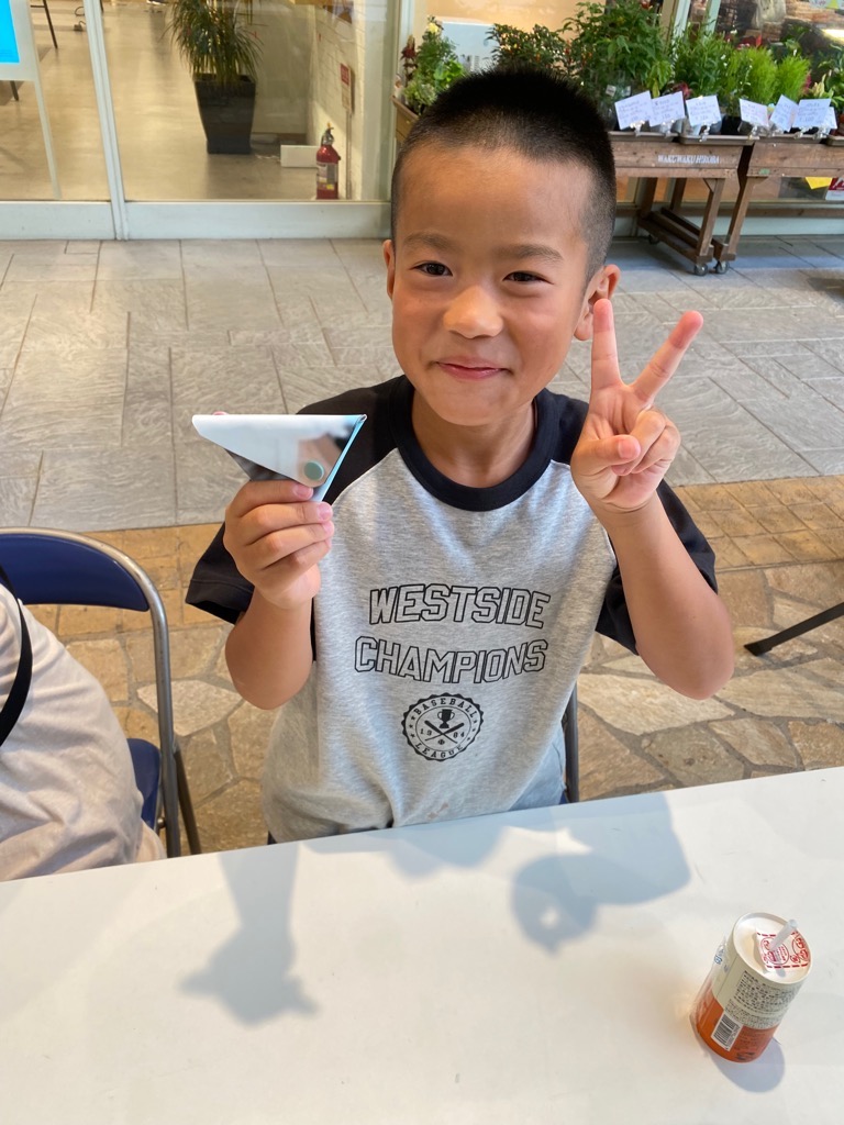 完成した小物ケースを持ち、笑顔でピースして写真撮影を受ける男子児童の様子