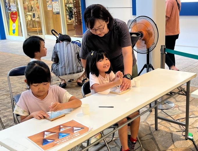 女子児童2人が切り取られた店舗バナーにキリを使用し、穴を開ける様子