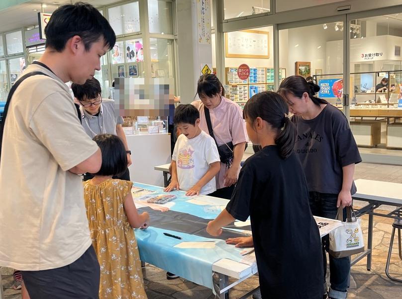 机に敷かれた店舗バナーを囲むこどもと保護者の様子