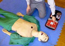 マネキン人形を横たわらせてAEDの準備をする男性の写真