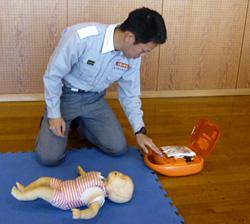 赤ちゃん人形をマットに寝かせてAEDの準備をする男性の写真
