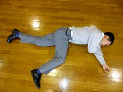 フローリングに足を開いて横向きに横たわる男性の写真