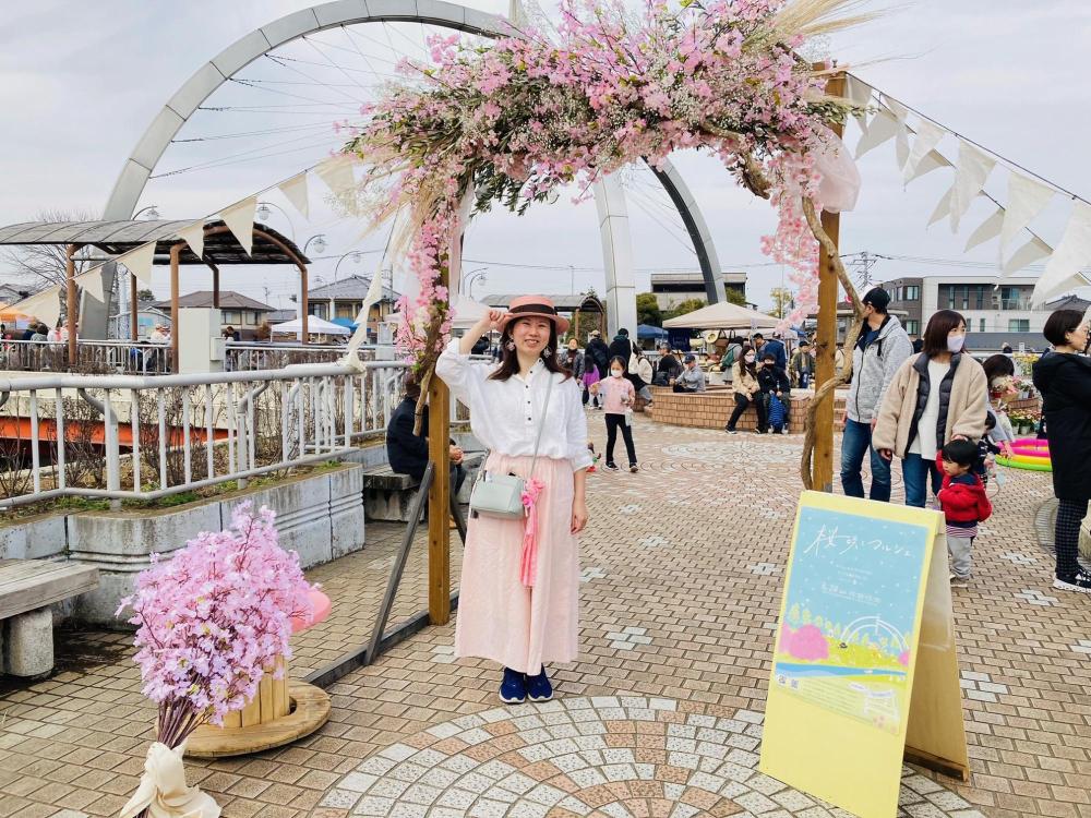 桜のゲートの前で帽子を被り満面の笑みを浮かべるナオナさん